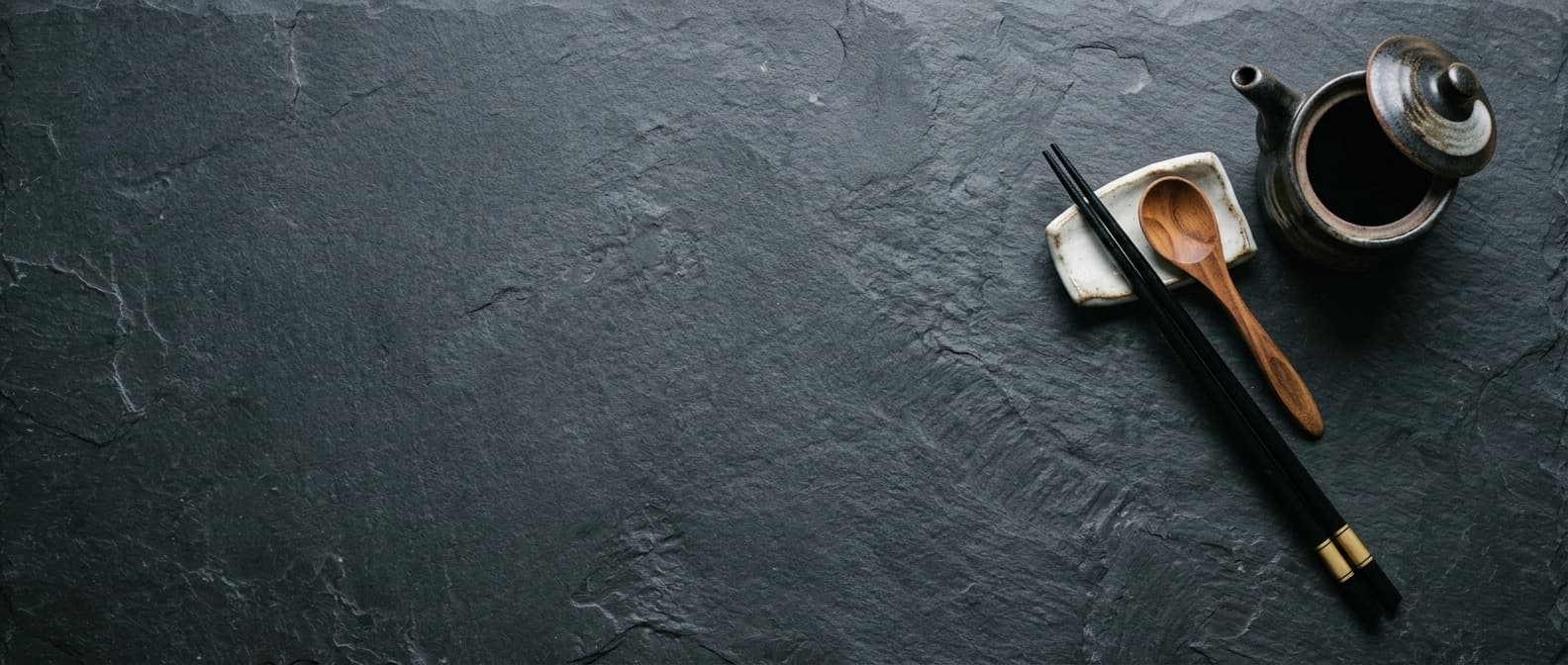 Chopsticks, a wooden spoon, and a soy pot on a dark stone counter